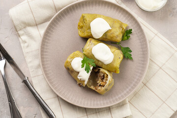 Three vegetarian cabbage rolls stuffed with rice, mushrooms, carrots and onions topped with vegan sour cream, traditional ukrainian dish during religious fasting time periods on a grey plate, top view