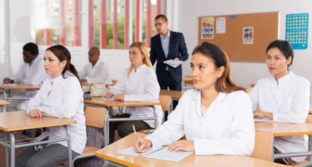 Fototapeta premium Medical students in white coats listen to a lecture in the audience