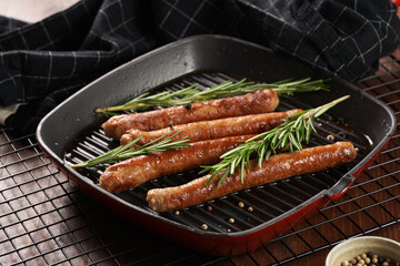 Traditional german organic pork sausages grilled on a red grill pan with rosemary branches and whole black pepper seeds on wooden background