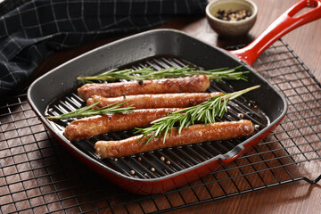 Traditional german organic pork sausages grilled on a red grill pan with rosemary branches and whole black pepper seeds on a baking rack on a wooden background