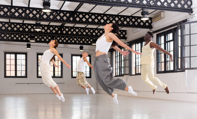 Group of positive sportive adults training in modern dance hall, jumping together