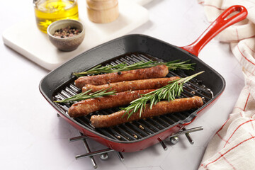 Traditional german organic pork sausages grilled on a red grill pan with rosemary branches and whole black pepper seeds on a marble background