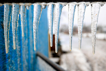Close up \of long icicles forming under a hand rail on the steps of a blue building