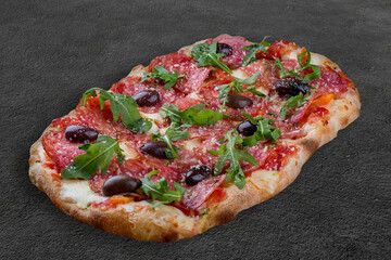 Pizza Diavolo with chorizo, rucola, jalapeno, chili, kalamata, pesto. Roman pizza rectangular on dark background