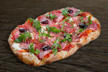 Pizza Diavolo with chorizo, rucola, jalapeno, chili, kalamata, pesto. Roman pizza rectangular on wood background