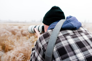 Over the shoulder view of a photographer in winter clothing composing his landscape shot with a...