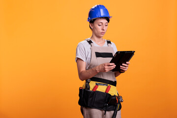 Portrait of woman industry engineer working with tablet, looking for renovating inspiration online on wireless gadget. Female contractor in overalls using electronic digital device.