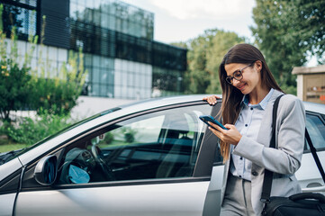 Business woman getting into the car and using smartphone