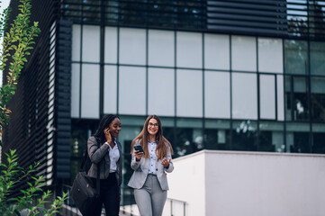 Two multiracial business woman meeting outside and using a smartphone