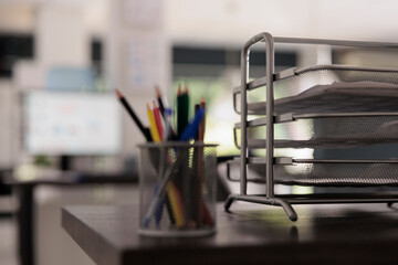 Close up view of metal pencil holder with colored pencils in creative design office, next to folder...
