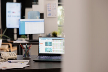 Partial view of modern empty office workplace with electronic devices displaying stock market investment data. Laptop on desk of financial company and investment risk advisor.