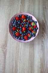 Pink rustic bowl filled with fresh blueberries and strawberries. Wooden background, top view.