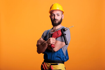 Happy building contractor holding power drill gun and posing in studio, looking at camera....