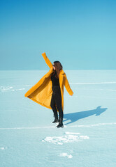 Young happy woman in yellow coat walking on snowy ice, freedom concept