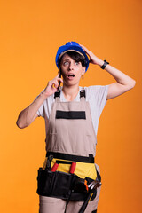 Worried stressed construction worker receiving bad news about renovating project delay, posing in studio. Female building contractor answering phone call over yellow background.