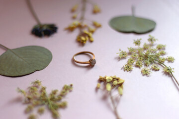 Engagement ring and pressed flowers. Pink background, selective focus.