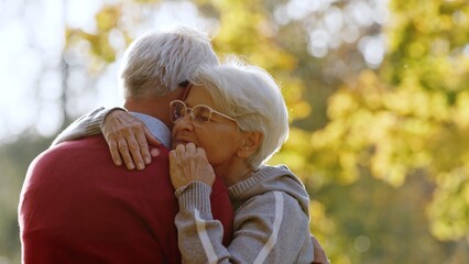 Fototapeta premium Two loving grey-haired people hugging outdoor in autumn nature. High quality photo