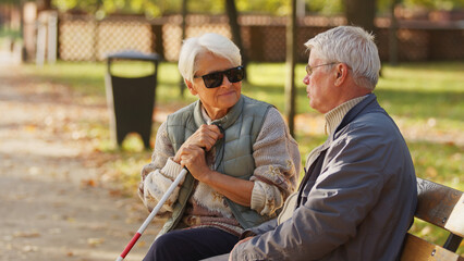 Obraz premium Blind elderly woman with her husband sitting on a bench in the park. High quality photo