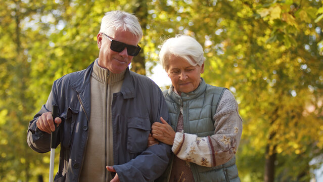 Senior married couple with blind man close together strolling through the park. High quality photo