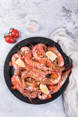 Baked langoustines in garlic sauce with cherry tomatoes on a black plate on a light marble background, top view. 