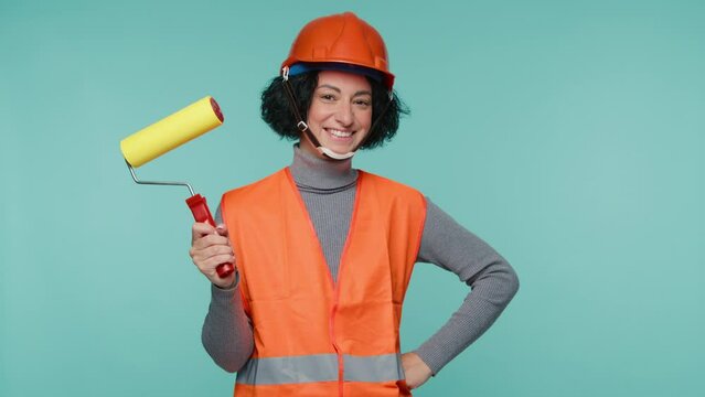 Portrait of professional painter woman with yellow roller at work on blue wall studio background. Offering professional painting services. 4K Stock video of professional painting services contractor