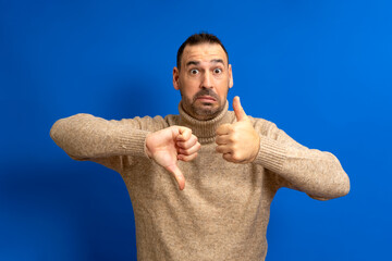 Bearded hispanic man wearing a turtleneck sweater giving a thumbs up and a thumbs down in a gesture...