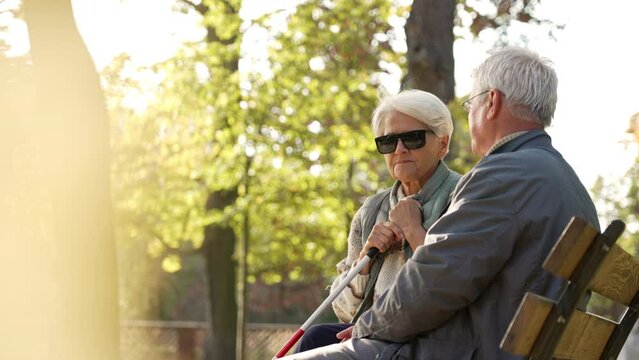 Blind elderly woman with dark sunglasses on with her husband in the park. High quality photo