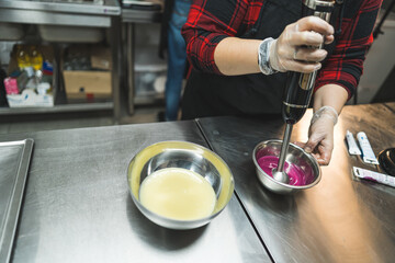 Unrecognizable female pastry chef prepares a pink icing for a cake, whips it with a blender in a stainless steel bowl. High quality photo