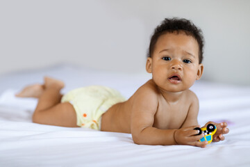 Adorable Little Black Baby Boy Lying On Bed And Holding Toy Car