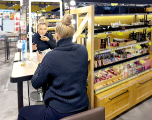 Woman buying make up at cosmetics section in store. choosing cosmetics, perfumes, creams and shampoos, Using tester.