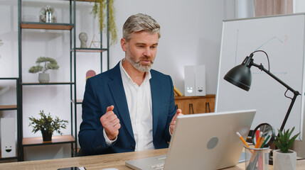 Mature businessman working on laptop computer at home office desk talk on online communication video call with employee, boss. Manager gray-haired old man freelancer support services looking at camera