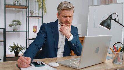 Stressed mature man feeling worried about problem analyzing information, read business papers...
