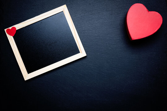 Photo frame and toy heart on a black background. Space for text. Congratulations on Valentine's Day.