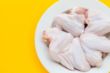 Fresh raw chicken wings in white plate on yellow background.
