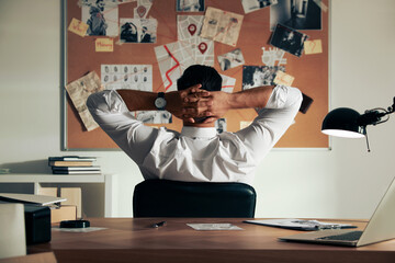 Detective looking at evidence board in office, back view