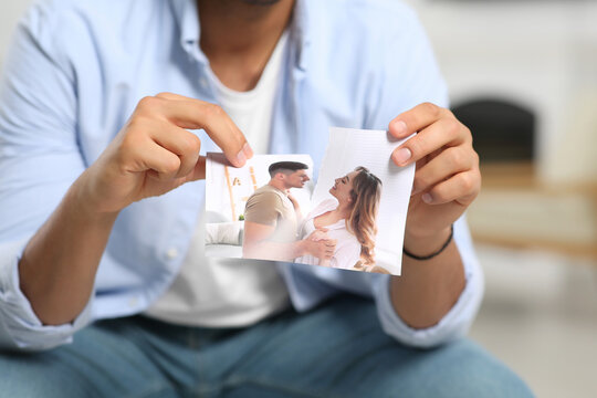 Man tearing photo indoors, closeup. Divorce concept