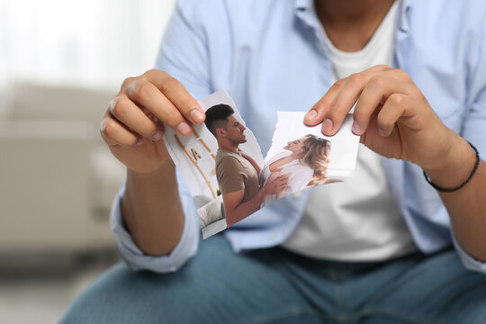 Man tearing photo indoors, closeup. Divorce concept