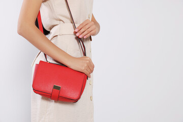 Woman with stylish red bag on light grey background, closeup. Space for text