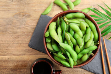 Green edamame beans in pods served with soy sauce on wooden table, flat lay