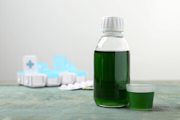 Bottle of syrup and measuring cup on wooden table against white background, space for text. Cold medicine
