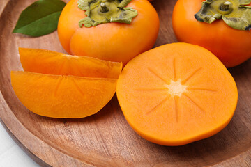 Delicious ripe persimmons and knife on white table, closeup