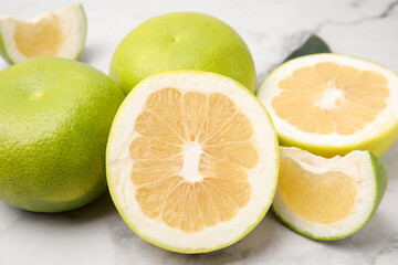 Whole and cut sweetie fruits on white marble table, closeup