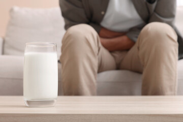 Man suffering from lactose intolerance at home, focus on glass of milk. Space for text
