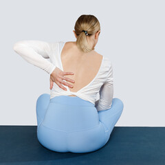 Back pain during yoga. A young woman rear view sits on a yoga mat and holding onto her sore back.