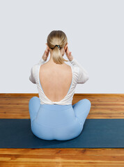 Head pain during yoga. A young woman rear view sits on a yoga mat and holding her sore head.