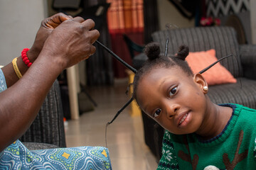 African stylist making new hair style on the head of a little Nigerian girl child