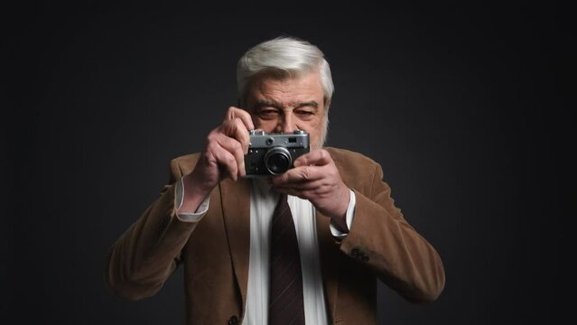 Close-up shot of retired man taking photos indoors. Portrait of adult man holding retro-styled camera and showing thumb up gesture. High quality 4k footage