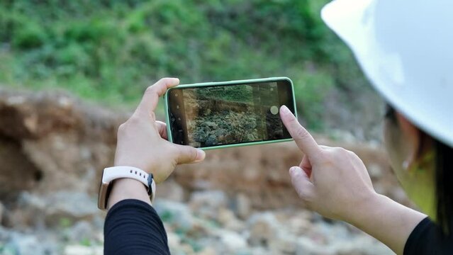 Female geologist using mobile phone to take pictures, examine nature and analyze rocks or pebbles. Researchers collect samples of biological materials. Environmental and ecology research.