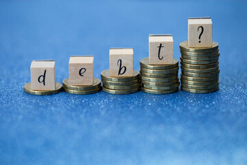 A Question of Debt. Debt spelled in letter blocks on piles of gold coins. Studio shot, blue background, no people.