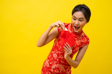 Beautiful Asian woman wearing traditional cheongsam with red envelope isolated on yellow background, Happy Chinese New Year.